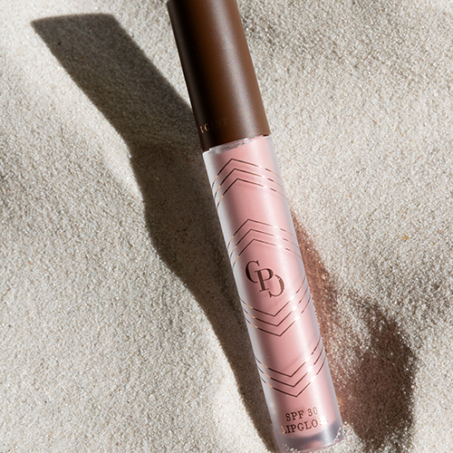 Sfeervolle opname van een Cent Pur Cent lipgloss SPF 30 Rose liggend in het zand.