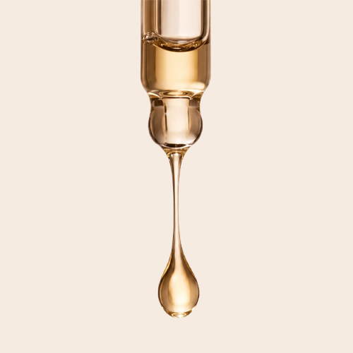 Close-up van een glazen pipet waar een druppel gouden serum uitdruipt om de textuur te tonen