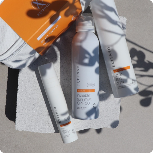 De Extenso Sun Care set bestaande uit de sun cover SPF 50, invisible sun mist SPF 50 en after sun care flacons op een lichte stenen ondergrond met schaduwen van bladeren.