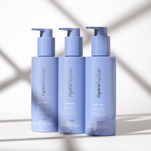 Drie flacons HydroPeptide Lumi Firm Glow-Inducing Tightening Lotion naast elkaar opgesteld in een sfeervolle setting met schaduwlijnen
