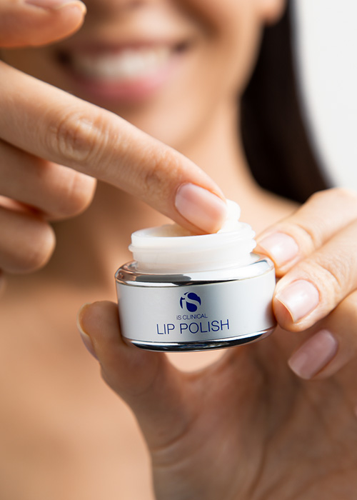 Close-up van een persoon die met de vinger een kleine hoeveelheid iS Clinical Lip Polish uit een potje haalt.