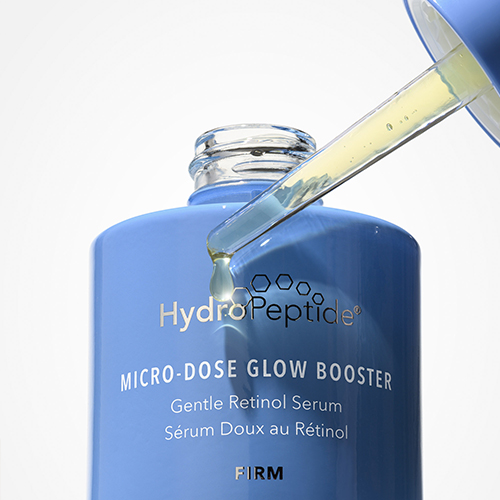 Een blauwe HydroPeptide Micro Dose Glow Booster flacon waarbij een druppel serum uit de glazen pipet valt.