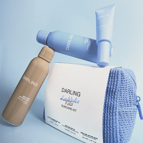Artistieke compositie van de Darling SPF 50 spray, After-Sun en Glowy Screen gegroepeerd rondom de blauwe toilettas.