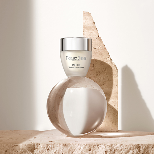 De Tensolift Neck Cream pot gepresenteerd op een glazen bol en natuursteen in een lichte setting.