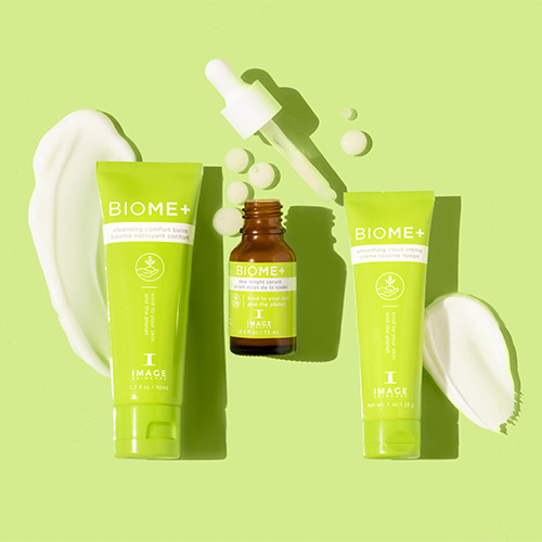 Bovenaanzicht van de BIOME+ Discovery Kit producten op een groene achtergrond, omringd door vloeibare texturen van de balsem, het serum en de crème.