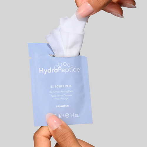 Handen die een resurfacing pad uit een HydroPeptide sachet halen