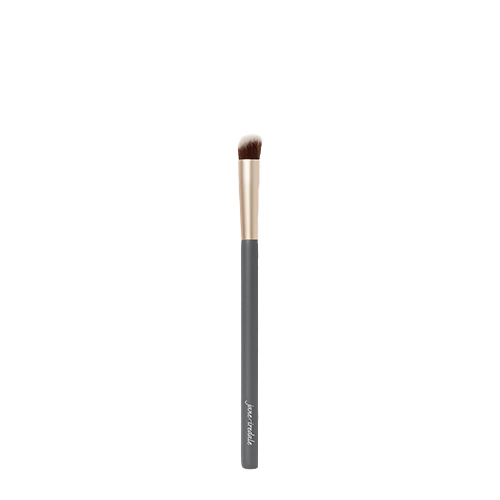 Een Jane Iredale Concealer Brush op een witte achtergrond. De kwast heeft een donkergrijze steel met het Jane Iredale logo, een goudkleurige huls en een schuin afgesneden borstelkop voor het nauwkeurig aanbrengen en blenden van concealer.