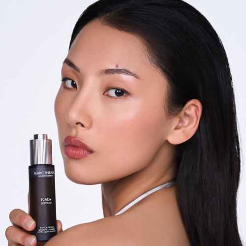 Model met lang haar houdt een flesje Marc Inbane NAD+ Booster serum vast naast haar gezicht