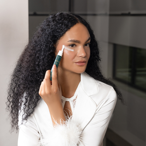 Een model brengt de EAVE Eye Empower oogcrème aan onder haar oog met de speciaal ontworpen applicator voor een verkoelend en verkwikkend effect.