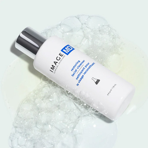 Een flacon van de IMAGE MD Restoring Facial Cleanser liggend in een wolk van wit reinigingsschuim.