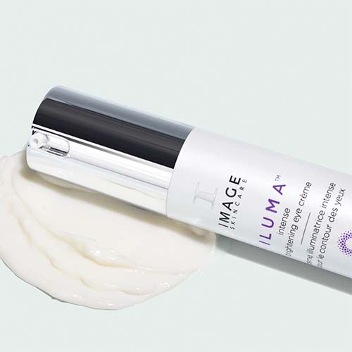De Image Skincare Iluma Intense Brightening Eye Crème flacon ligt horizontaal op een decoratieve uitsmering van de witte oogcrème.