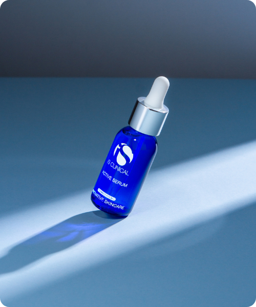 Een blauw flesje iS Clinical Active Serum met een pipetdop op een blauwe ondergrond met schaduw
