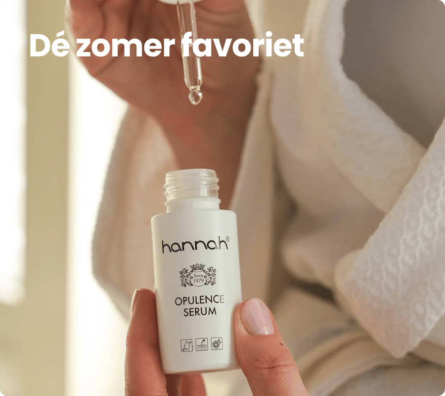 Een persoon in een witte badjas houdt een flesje hannah opulence serum vast terwijl er een druppel uit een pipet valt met de nederlandse tekst dé zomer favoriet