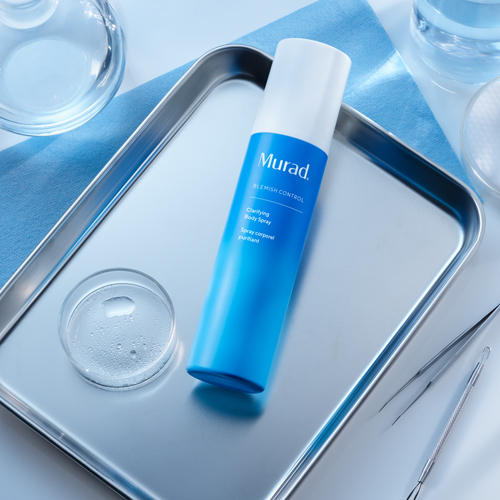Murad Clarifying Body Spray op een zilveren schaal omringd door laboratoriumaccessoires