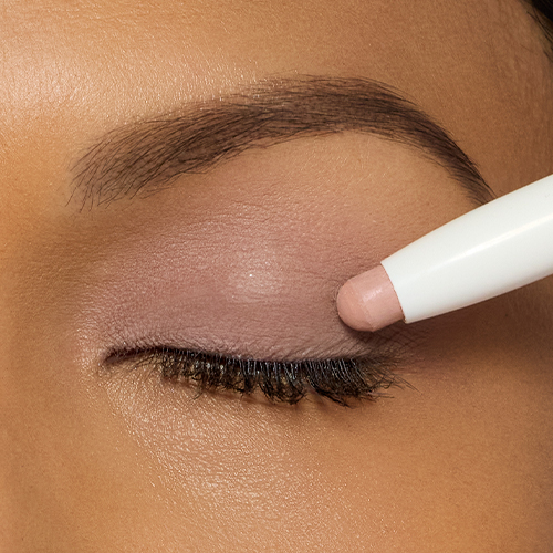 Close-up van een ooglid waarop de matte, zachtroze Cameo oogschaduwstick wordt aangebracht.