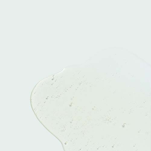 Detailopname van een transparante druppel Ageless serum met AHA-zuren op een glad oppervlak.