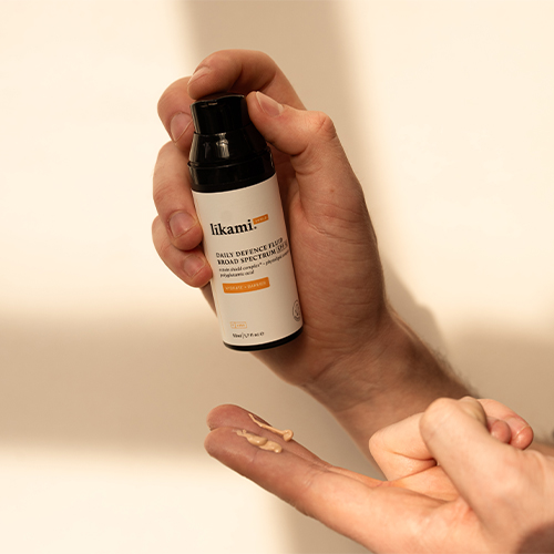 Een hand die op de pomp van de Likami flacon drukt, terwijl er twee kleine druppels van de vloeistof op de vingers van de andere hand liggen.