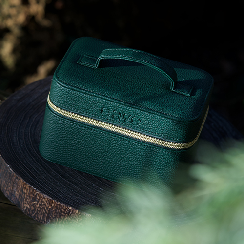 De groene EAVE Mini Vanity Bag gepresenteerd op een houten ondergrond in een sfeervolle buitenomgeving met natuurlijk licht.