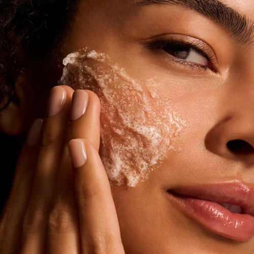 Close-up van een model dat een exfoliërende iS Clinical gezichtsscrub met fijne korreltjes aanbrengt op haar wang