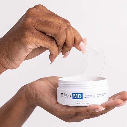 Close-up van een hand die met een pincet een hydrogel oogmasker uit de IMAGE MD pot haalt.