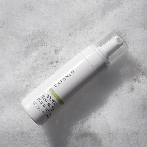 Witte flacon Extenso Impurity Cleansing Mousse in een bad van reinigend schuim.