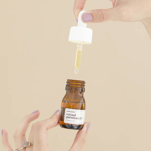 Handen die een druppelflesje Prescription retinol palmitate vasthouden met een druppel aan de pipet