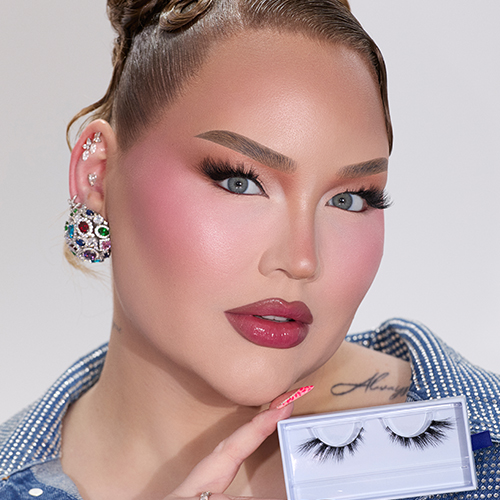 Nikkie de Jager, bekend als NikkieTutorials, kijkt in de camera met volledige make up, waaronder donkere nepwimpers, en houdt een doosje Nimya wimpers vast.