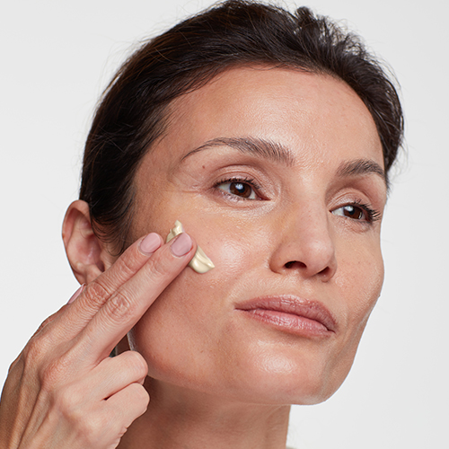 Een close-up van een vrouw die HydroPeptide Collagen ReActivate AM crème aanbrengt op haar gezicht.
