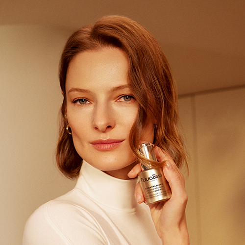 Een model met een natuurlijke uitstraling die het Natura Bisse Essential Shock Intense Retinol Night Renewal serumflesje vasthoudt bij haar gezicht.