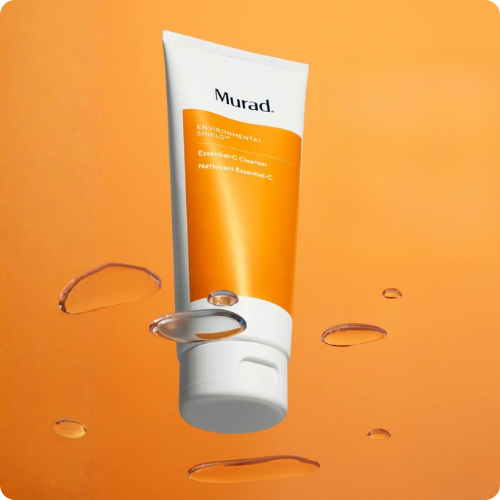 Close-up van een tube Murad Essential C Cleanser op een warme oranje ondergrond met waterdruppels
