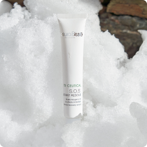 Een witte tube van Natura Bissé NB-Ceutical S.O.S. Instant Rescue serum staat rechtop in een berg witte sneeuw. De afbeelding heeft afgeronde hoeken.