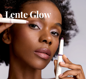 Een vrouw toont een frisse make-uplook met glanzende oogschaduw terwijl ze twee Jane Iredale oogschaduw sticks vasthoudt de kleur roze en paars. De tekst 'Hallo... Lente Glow'