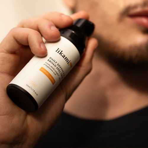 Een man houdt de Likami Hydrate + Barrier flacon vast, klaar om het product aan te brengen als onderdeel van zijn huidverzorgingsroutine.
