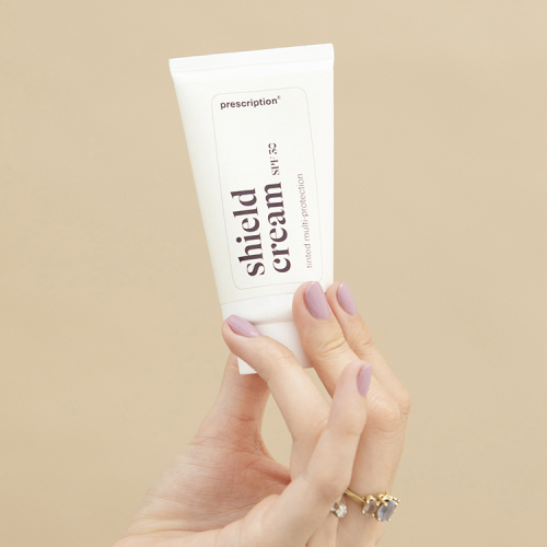 Hand die een tube Prescription shield cream spf 30 omhoog houdt