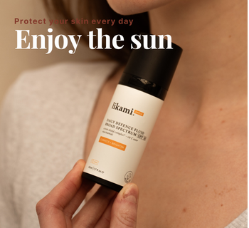 Een vrouw houdt een fles Likami Daily Defence Fluid SPF 50 vast. De tekst op de afbeelding luidt: "Protect your skin every day. Enjoy the sun."
