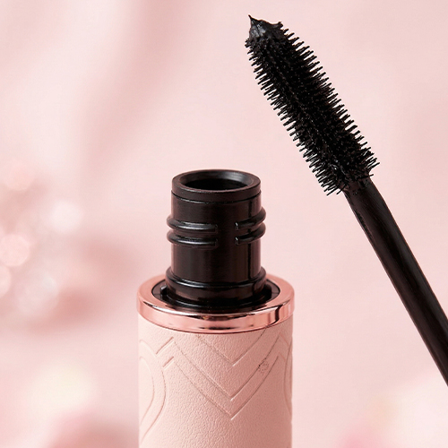 Een close-upfoto van de borstelharen van een Cent Pur Cent-mascara, die op een roze achtergrond ligt.