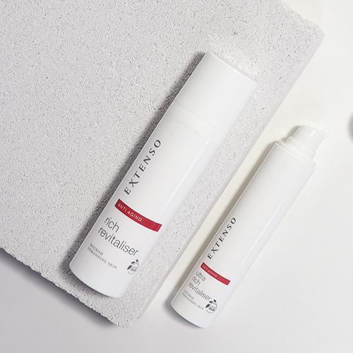 Twee witte flacons van de Extenso rich revitaliser en ultra rich revitaliser liggend op een lichtgrijze stenen ondergrond