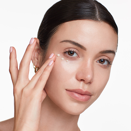 Close-up van het gezicht van een vrouw die stipjes oogcrème van HydroPeptide onder haar oog aanbrengt met haar vingertop.