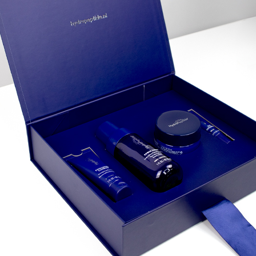 Een open donkerblauwe geschenkdoos van HydroPeptide met daarin de inhoud en een blauw lint op een lichte ondergrond