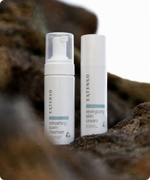 Twee flessen Extenso For Men huidverzorging, de refreshing foam cleanser en energizing skin cream, geplaatst op een rotsachtige ondergrond.