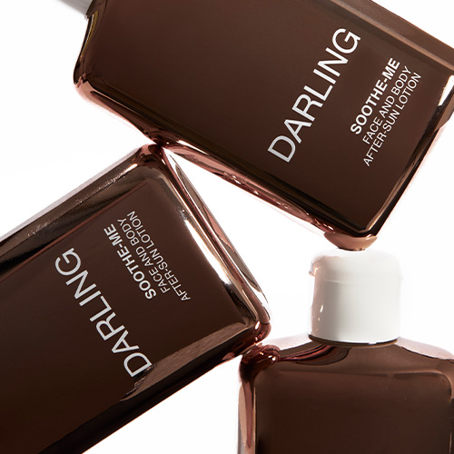 Een close-up van drie glanzende Darling Soothe Me After-Sun flacons die speels over elkaar heen liggen, waarbij de focus ligt op de witte typografie en de reflecterende metallic finish.