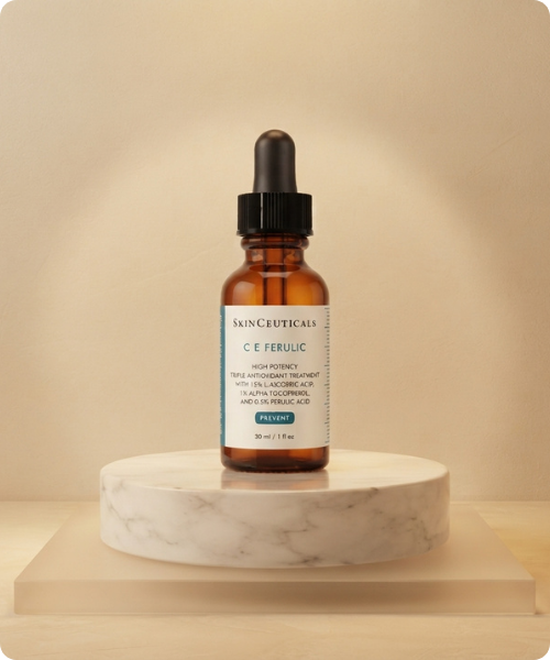 Een glazen flesje SkinCeuticals C E Ferulic antioxidant serum met pipet, gepresenteerd op een ronde marmeren sokkel tegen een warme neutrale achtergrond.
