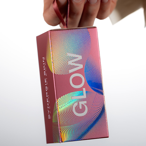 Hand die een roze Synergie Skin Glow geschenkdoos met lint vasthoudt