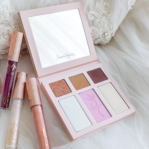 Sfeerfoto van het open Cent Pur Cent Coup de Foudre Palette d Amour, geplaatst op een witte kanten achtergrond naast bijpassende lipglosses van hetzelfde merk.