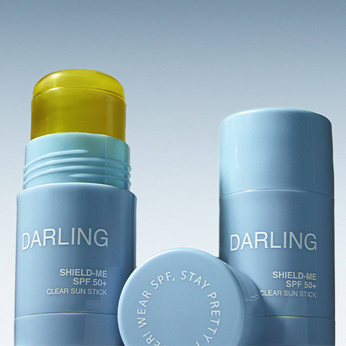 Twee lichtblauwe Darling zonnebrandsticks, één geopend en één gesloten, stijlvol gepresenteerd tegen een zachte blauw-grijze achtergrond.