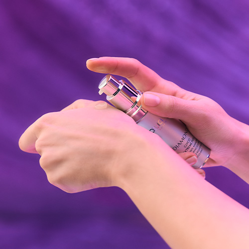 Close-up van handen die de zilveren Glyco Extreme Peel flacon vasthouden en een druppel van het product op de rug van de hand aanbrengen.