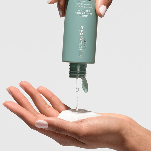 Vloeistof die uit een flesje van HydroPeptide Liquid Resurfacing Solution op een hand druppelt