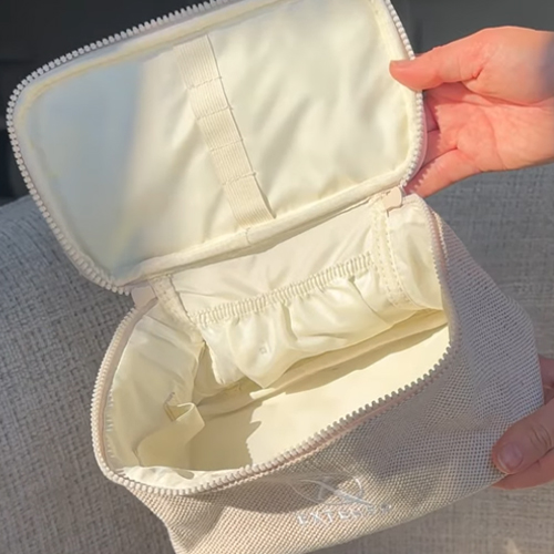 Een geopende, crèmekleurige beauty case van het merk Extenso. De tas is gemaakt van een geweven stof en heeft een lichte binnenvoering met elastische vakken en lussen om make-up en verzorgingsproducten georganiseerd op te bergen.