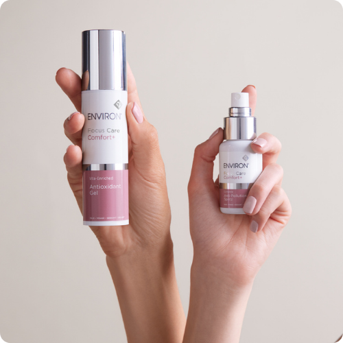 Twee flacons van de Environ Focus Care Comfort+ lijn, de Vita-Enriched Colostrum Gel en de Anti-Pollution Spritz, liggend op een spiegelende ondergrond.