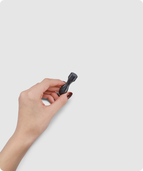 Een hand houdt de kleine, donkergrijze Environ Cosmetic Focus-CIT stempel vast tegen een lichtgrijze achtergrond